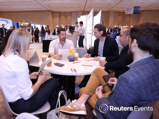 A group of senior professionals engaged in a focused, collaborative roundtable discussion at a Reuters Events conference, capturing the intimate, peer-to-peer knowledge sharing and high-level strategic problem-solving that defines the event experience.