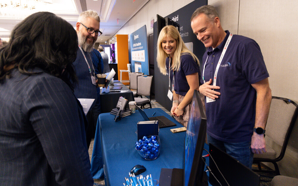 Smiling event sponsors interacting with attendees at a promotional exhibition booth during a Reuters Events conference.
