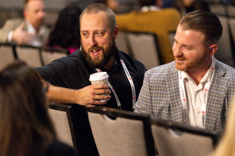 Two male attendees smiling and chatting during a networking break at a Reuters Events conference, with one holding a coffee cup.