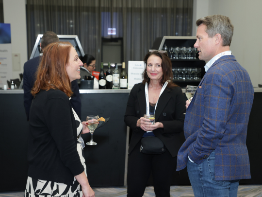 Three Total Health conference attendees chat over drinks during an evening reception.