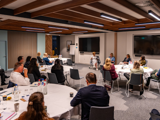 Wide view of Supply Chain Europe conference attendees seated at round tables beneath a striking wooden ceiling, taking part in a presentation.