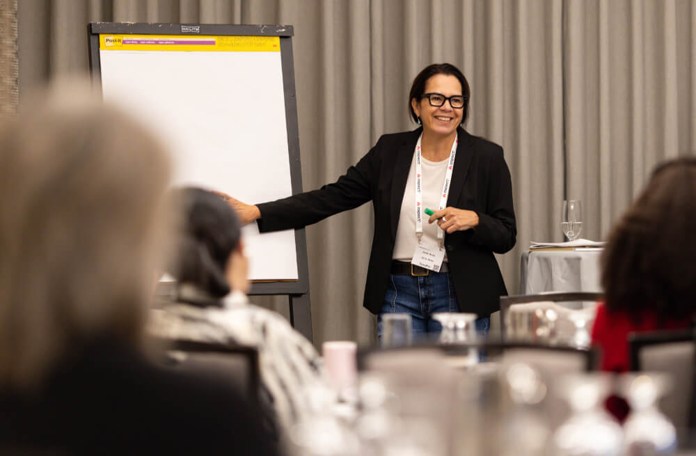  A female presenter smiling and gesturing toward a whiteboard during an interactive workshop session at a Reuters Events conference.
