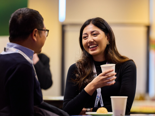 Two Reuters Pharma event attendees chat informally, with one woman smiling while holding a paper cup