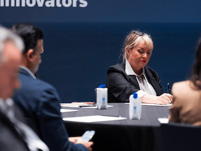 A focused female delegate taking notes during a deep-dive roundtable session at a Reuters Events conference, highlighting the intellectual engagement and strategic work that defines the attendee experience.