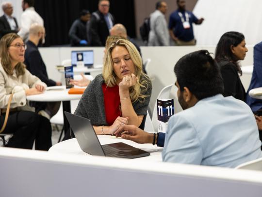 Female executive say at a table with a male executive networking with a laptop between them at Reuters Events Pharma USA 2026