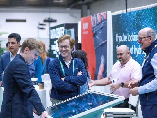 Attendees laugh and interact with a touchscreen kiosk at an expo booth during the Energy LIVE scavenger hunt, with hydrogen and data center exhibitor banners visible.