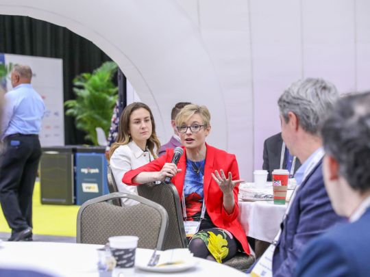 A woman in a red blazer speaks animatedly into a microphone during a roundtable discussion at Energy LIVE.