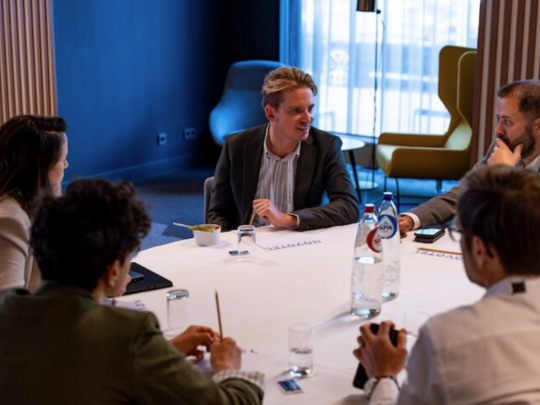 A group of insurance professionals engaged in focused discussion around a roundtable, with one man leading the conversation in a modern meeting room