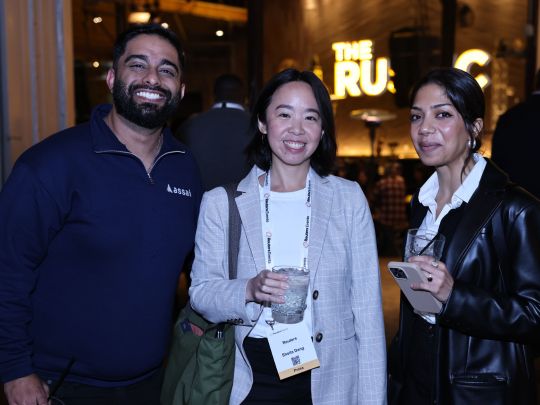 Three attendees smile together holding drinks at an evening networking reception during Energy LIVE.