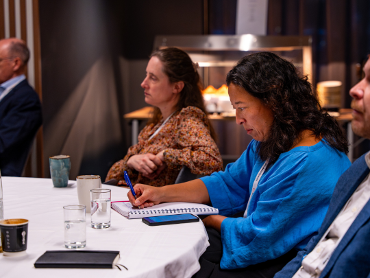 Attendees seated at a roundtable session at Supply Chain Europe, with a delegate in a blue top taking notes in a notebook during the discussion.