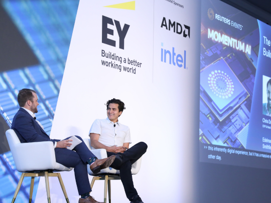 Two speakers in conversation on the Momentum AI stage, with EY, AMD and Intel sponsor branding behind them.