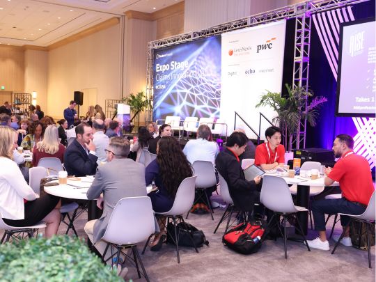 A bustling networking and exhibition hall at The Future of Insurance 2026. Attendees are seated at round tables near the Expo Stage, with prominent backdrops displaying major industry sponsors like PwC and LexisNexis.
