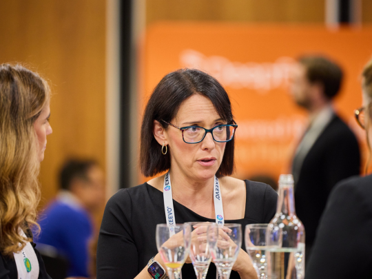A participant speaks with colleagues during the Women in Pharma breakfast workshop, seated at a table with water glasses and name lanyards. 