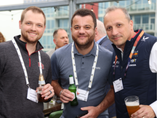 Three Connected Claims USA attendees hold drinks and pose together during a networking reception.