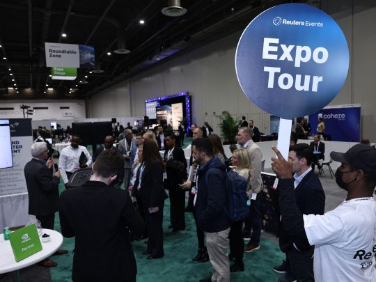 An Energy LIVE staff member holds up an 'Expo Tour' sign while guiding a group of attendees through the exhibition hall.