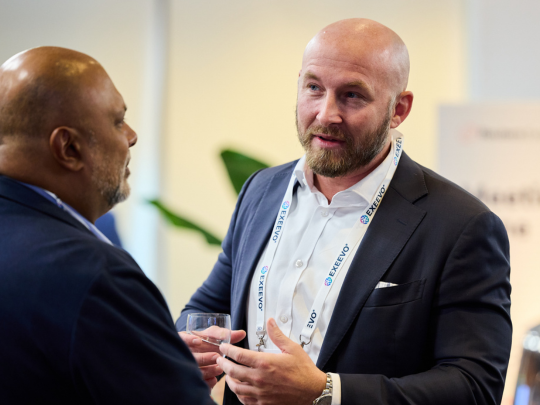 Two attendees in conversation at a Reuters Pharma event, including a man in a dark suit and event lanyard gesturing as he speaks
