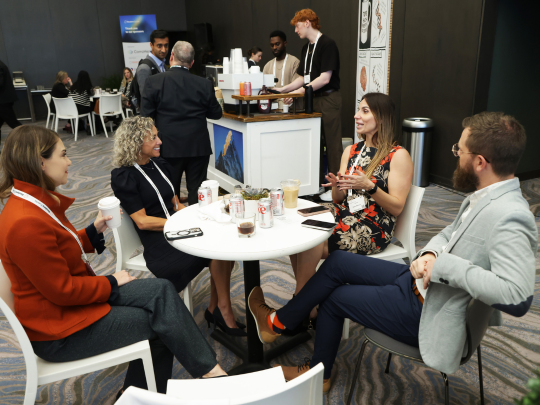 Four Total Health attendees sit around a café table, talking and networking during a break.
