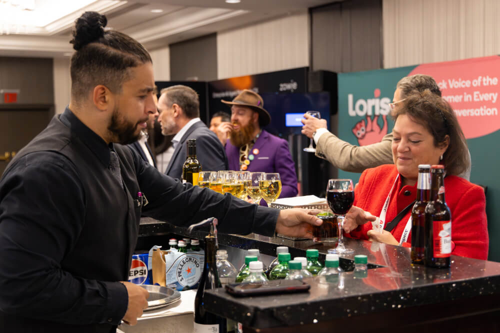 A bartender serving a cocktail to a female attendee at a lively evening networking reception during a Reuters Events conference.