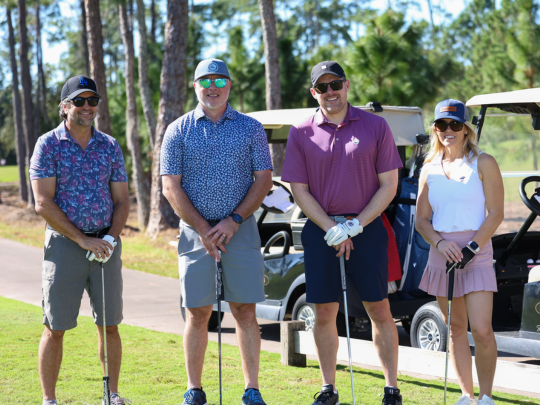 Attendees pose with golf clubs beside golf carts during a Connected Claims USA golf networking event.