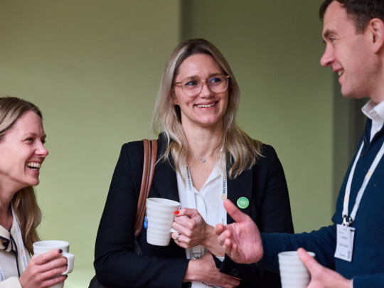 Three Energy Transition Europe delegates chatting and laughing over coffee during a networking break.