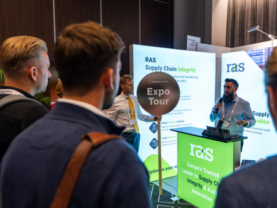 Attendees on an Expo Tour stop at the RAS Supply Chain Integrity exhibition stand at Supply Chain Europe, with a presenter demonstrating solutions at the booth.