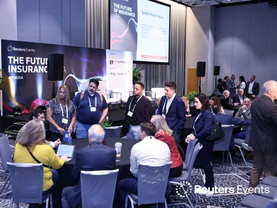 Insurance leaders networking at tables in a premium event hall during The Future of Insurance 2026 conference. Large stage banners display 'The Future of Insurance USA' and showcase sponsor logos including EY.