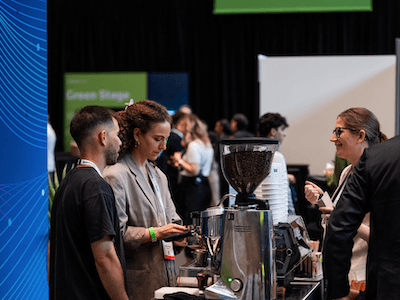 Two attendees sharing a casual, focused conversation at a conference coffee station, illustrating the high-quality, organic networking opportunities that occur throughout a Reuters Events conference.